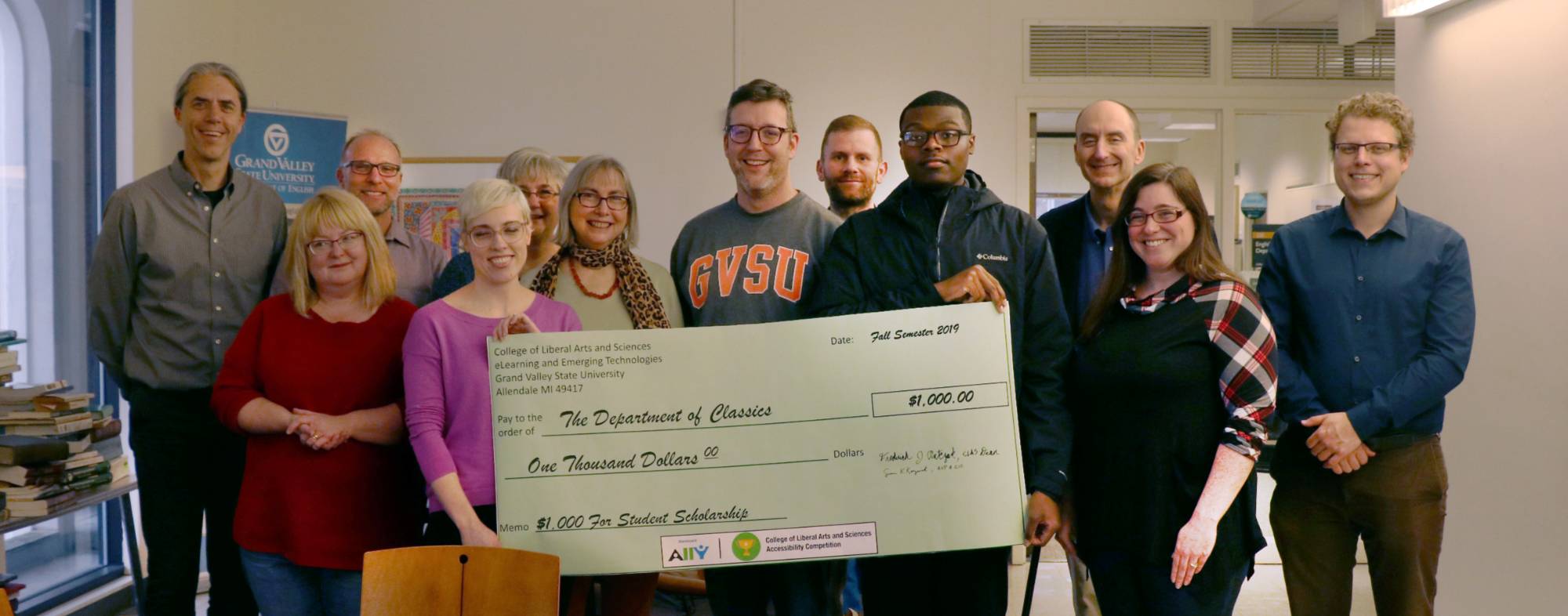 The department of classics staff are pictured holding a large poster check with a total amount of $1,000. The memo of the check is labeled: $1,000 For Student Scholarship